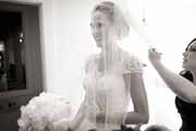 A candid black and white photo of a bridesmaid helping a bride with her veil.
