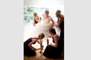 Bridesmaids help bride step into wedding shoes.