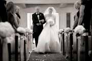 A black and white photo a father walking the bride down the aisle of Carmel Presbyterian Church at her wedding. 