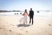 Newlyweds stroll away from camera on Garrapata State Beach in Big Sur.