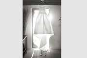 A black and white photo of a wedding gown hanging in a doorway.