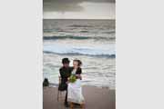 Candid portrait of bride sitting in groom's lap by ocean.