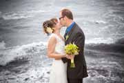 Newlyweds kiss during wedding ceremony by ocean.