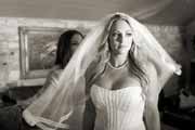 Black and white photo of bride putting veil on.