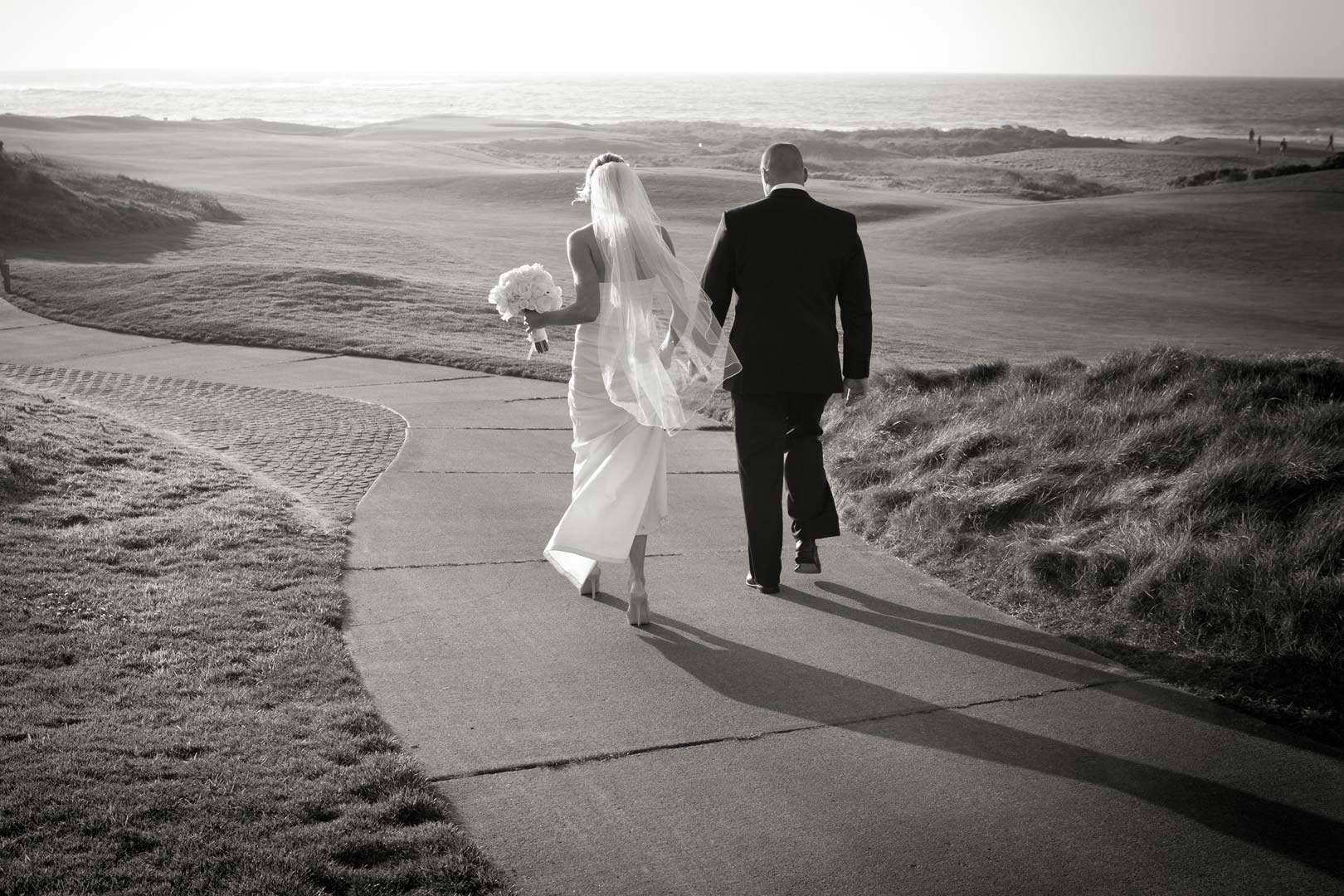 A black and white photo of a bride and groom walking away at the Inn at Spanish Bay in Pebble Beach.