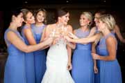 Bridesmaids with blue dresses toast bride with champagne.