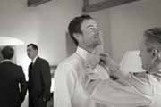 Black and white photo of groom tying bow tie.