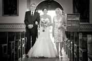 Black and white photo of bride and parents walking down San Carlos Cathedral aisle.