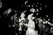 Black and white photo of flower petals tossed at newlyweds departing wedding reception.