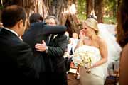 Groom hugs bride's father during redwood forest wedding ceremony.
