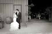 Black and white photo of newlyweds kissing outside wedding reception at Santa Lucia Preserve barn.