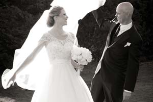 A black and white photo of a groom playing with his bride's veil.