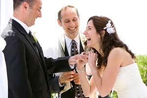 A laughing bride puts ring on groom's finger during wedding ceremony.